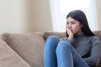close up face unhappy asian pretty young woman sitting alone couch