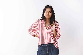 well not bad. portrait of impressed girlfriend pursing chin and squinting as showing okay gesture checking out great job of friend, giving approval and liking awesome project over white background